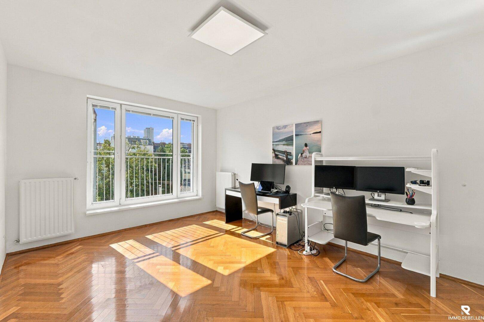 Helles Arbeitszimmer mit Fischgrätparkett, zwei Schreibtischen und großem Fenster.