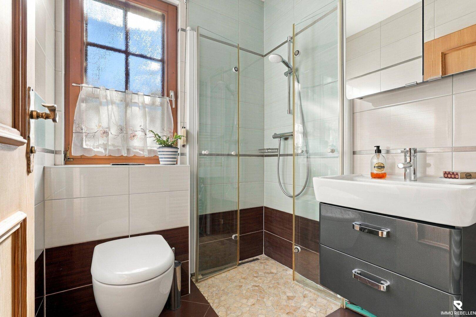 Modernes Badezimmer mit Duschkabine, Waschbecken und Fenster für Tageslicht.