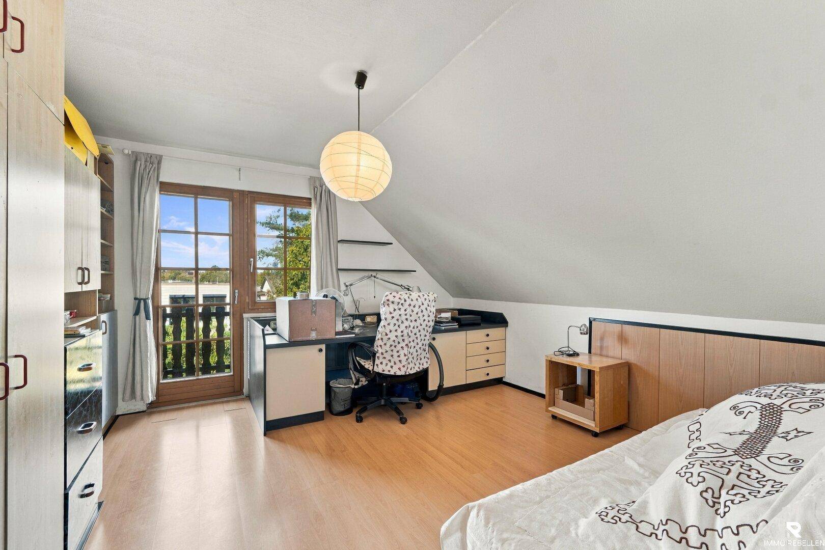 Schlafzimmer mit Holzboden, Schreibtisch und Balkonzugang, ideal als Arbeits- oder Gästezimmer.
