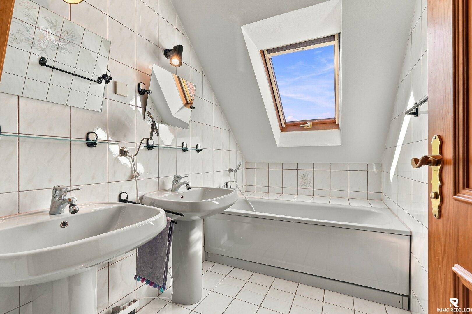 Helles Badezimmer im Dachgeschoss mit Badewanne, zwei Waschbecken und Dachfenster.