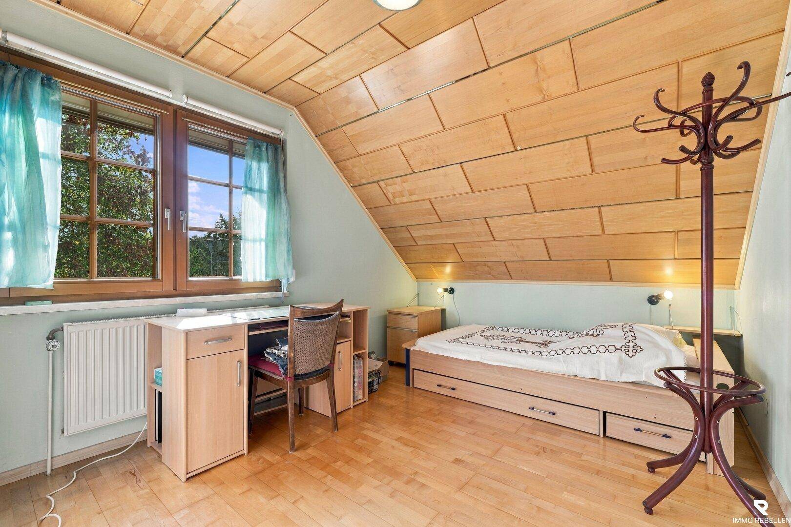 Helles Schlafzimmer im Dachgeschoss mit Holzdecke, Einzelbett und Fenster mit Blick ins Grüne.