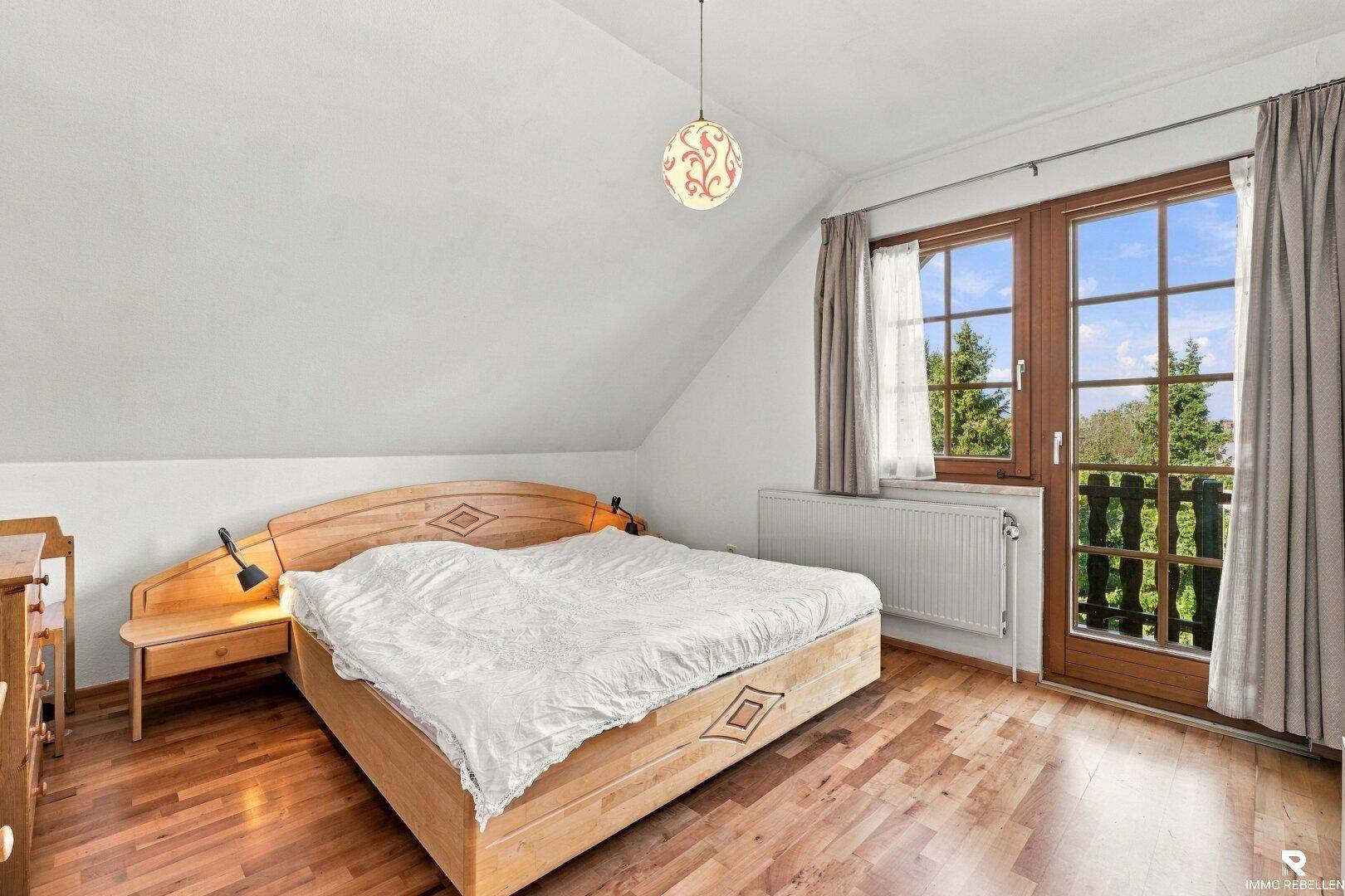 Gemütliches Schlafzimmer mit Holzbett, Parkettboden und Zugang zum Balkon mit grüner Aussicht.