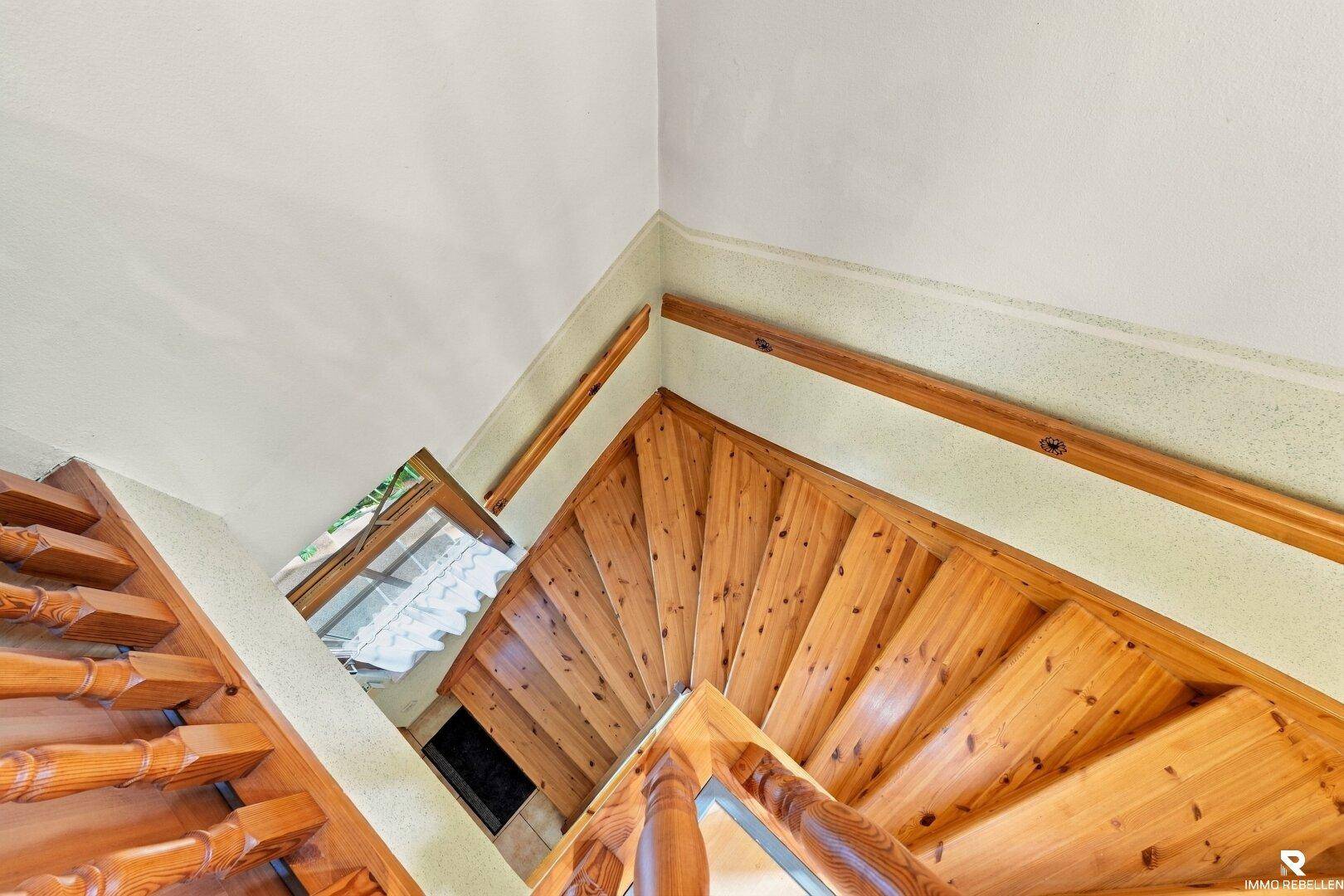 Holztreppe führt in die oberen Stockwerke, mit natürlichem Lichteinfall von oben.