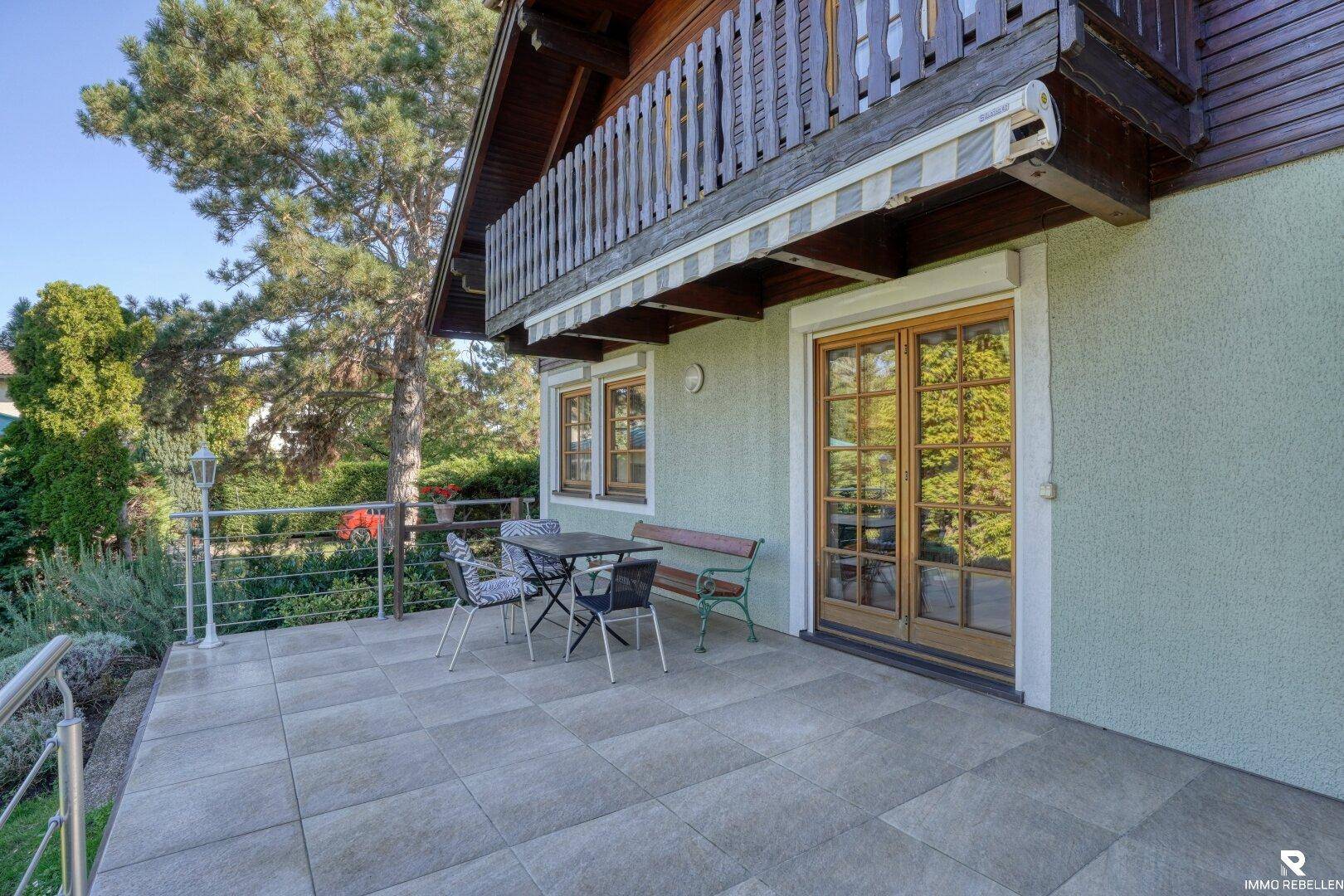 Sonniger Terrassenbereich mit Fliesenboden, Gartenmöbeln und Zugang zum Haus.