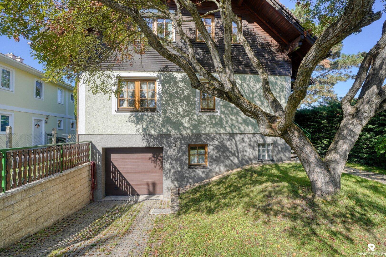 Seitenansicht des Hauses mit Garagenzufahrt und einem großen, alten Baum im Vorgarten.