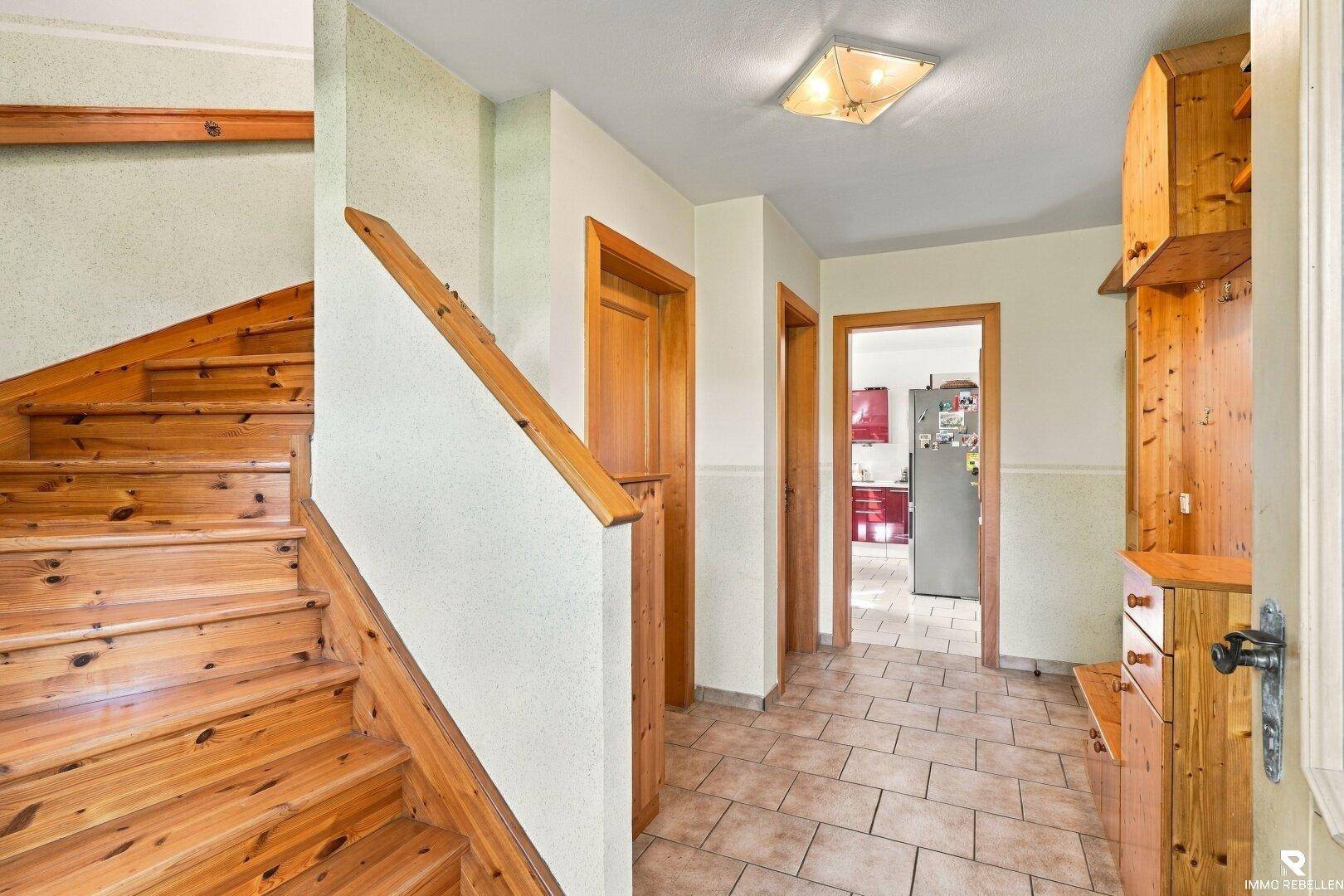 Heller Eingangsbereich mit gefliestem Boden, Holztreppe und Zugang zur Küche.