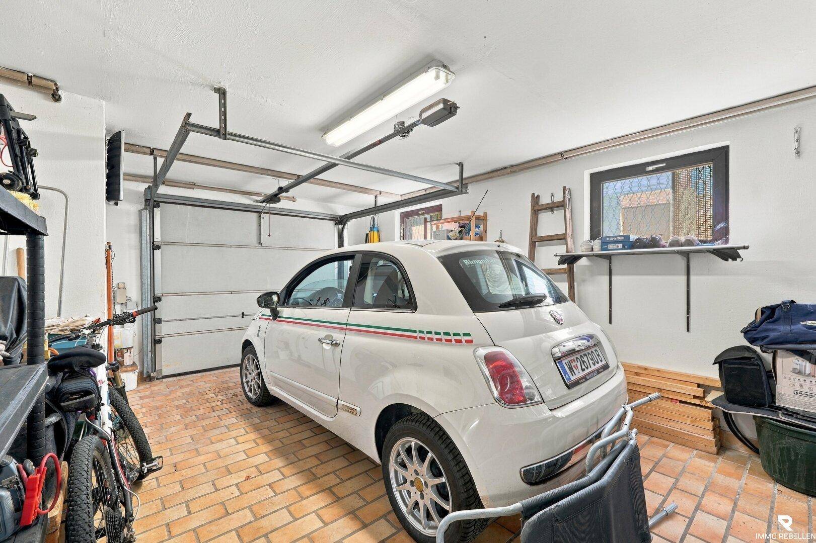 Geräumige Garage mit einem geparkten Auto, Rolltor und einem Fenster für Tageslicht.