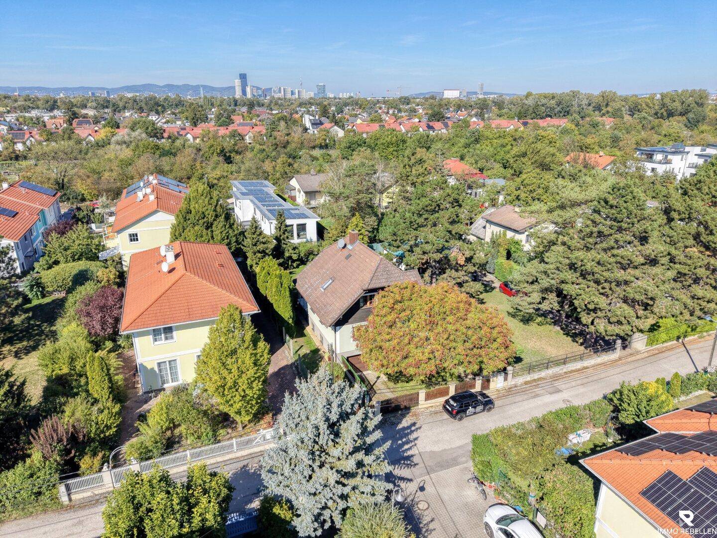 Panoramablick aus der Vogelperspektive auf die grüne Wohnsiedlung mit städtischer Skyline am Horizont.