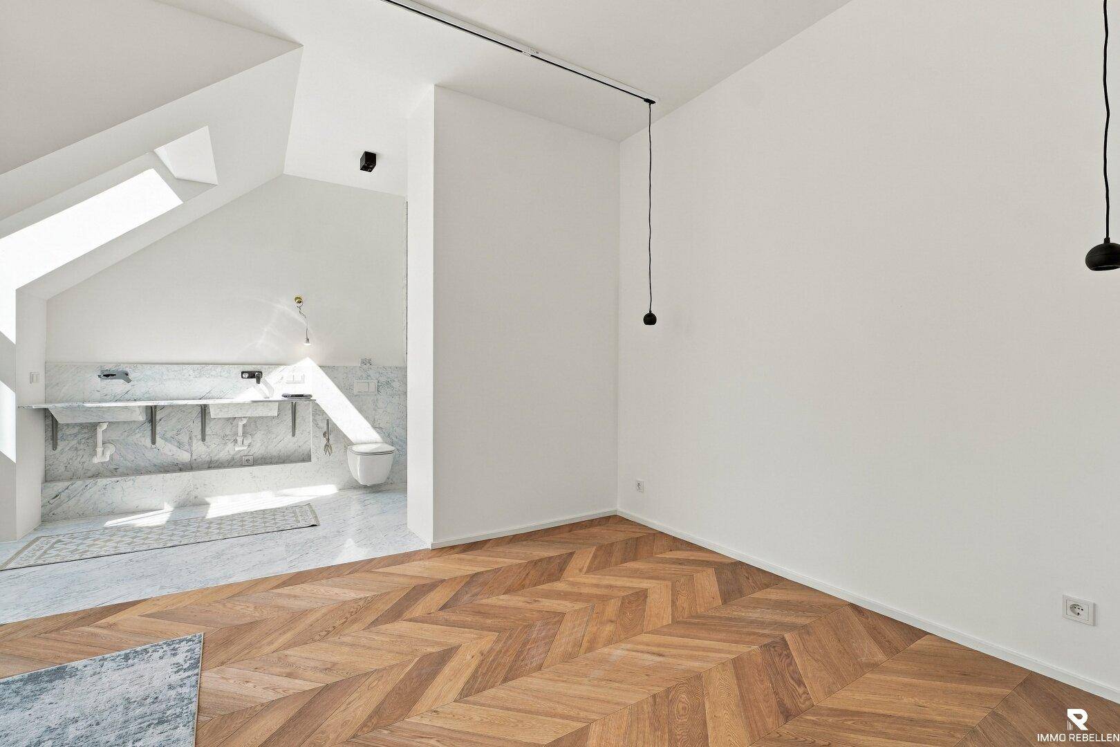 Geräumiges Zimmer mit Fischgrätparkett und Dachschrägen, angrenzend an ein modernes Badezimmer.