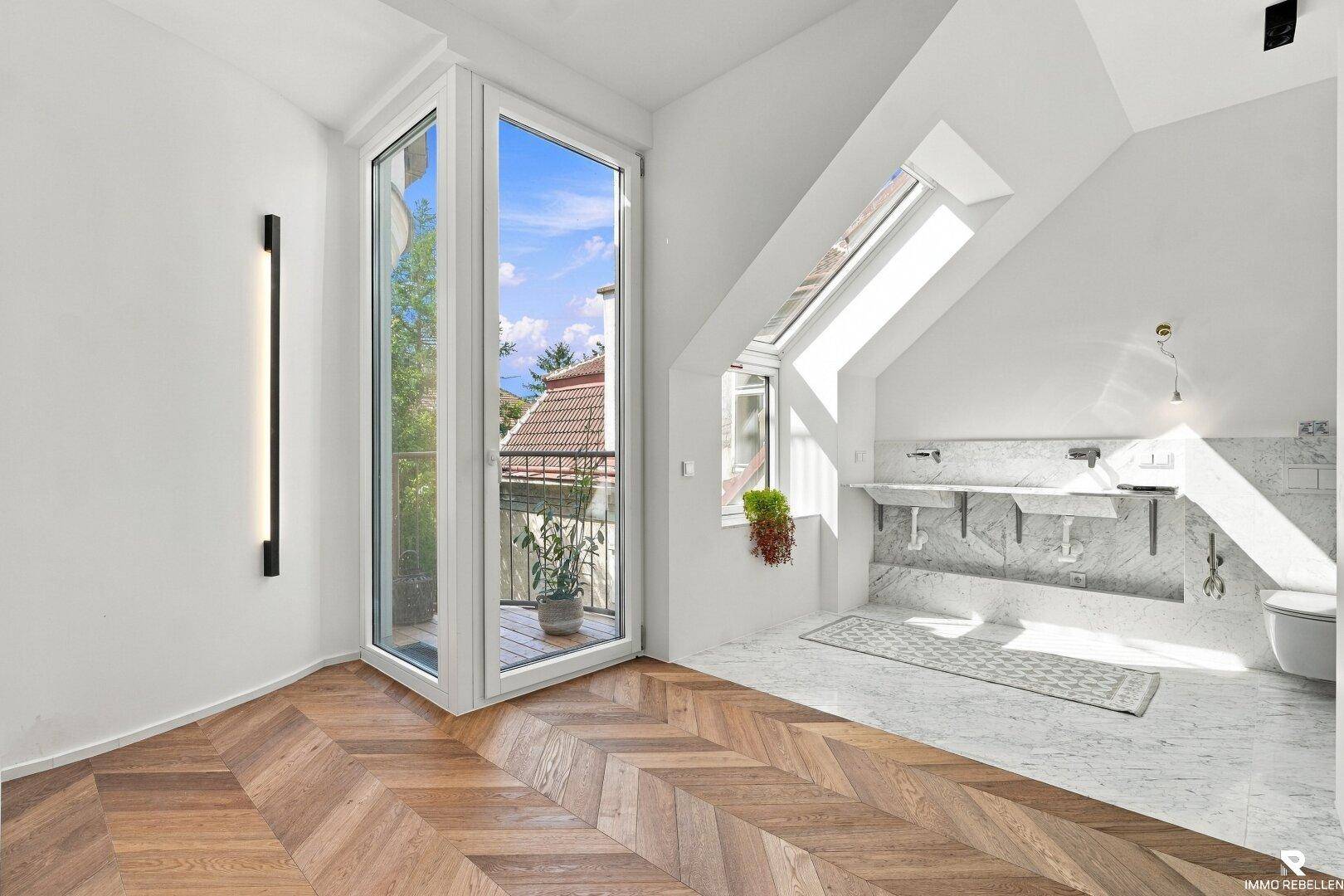 Heller Raum mit Fischgrätparkett, Dachschrägen und Zugang zu einem kleinen französischen Balkon.