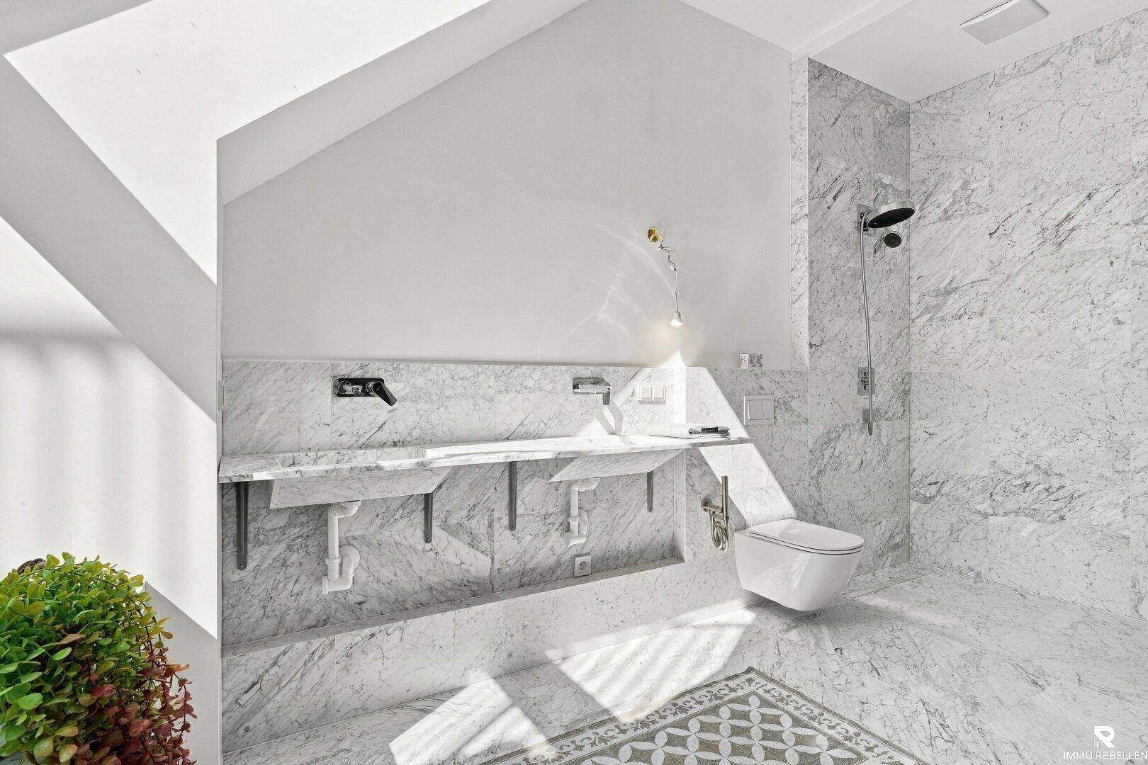 Elegantes Badezimmer mit Marmorfliesen, Doppelwaschbecken und moderner Dusche unter Dachschrägen.