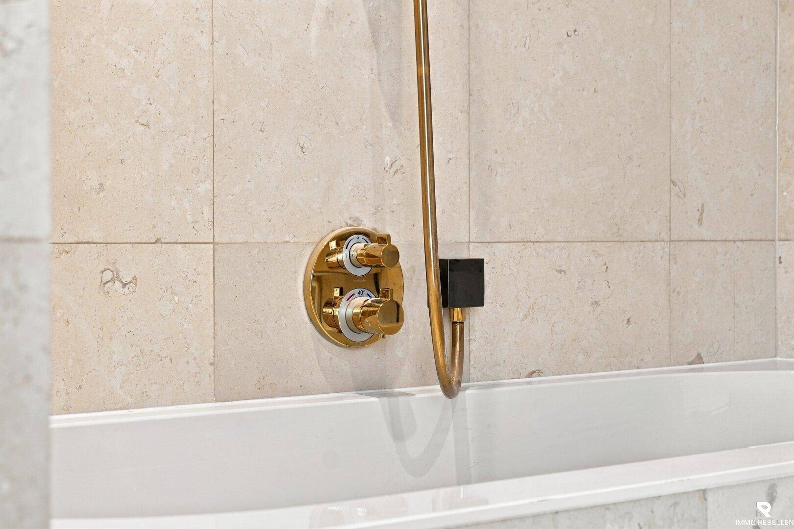 Detailaufnahme einer goldfarbenen Armatur über einer Badewanne in einem modernen Badezimmer.