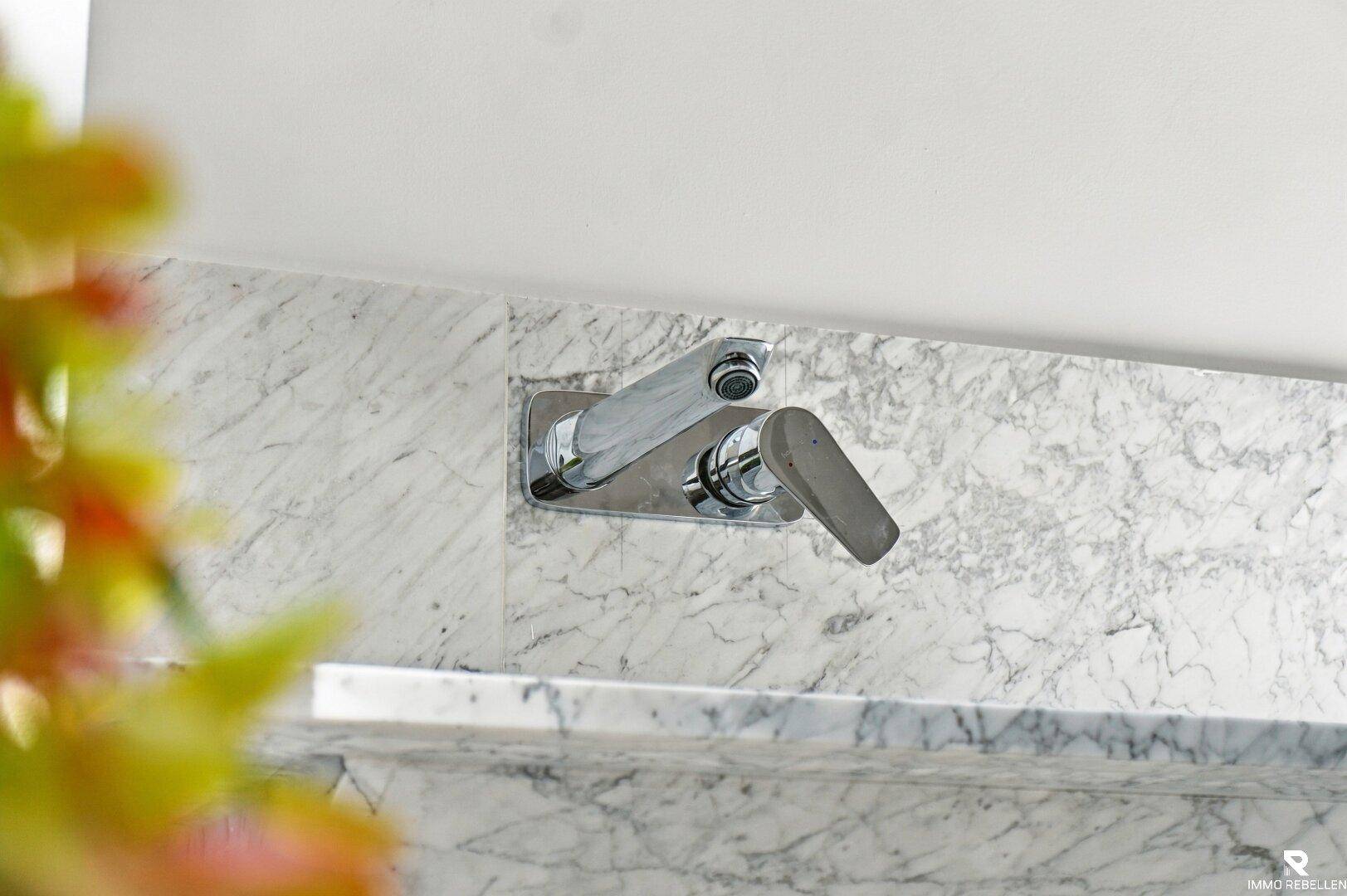 Detailaufnahme eines modernen Wandwasserhahns über einer Marmoroberfläche im Badezimmer.