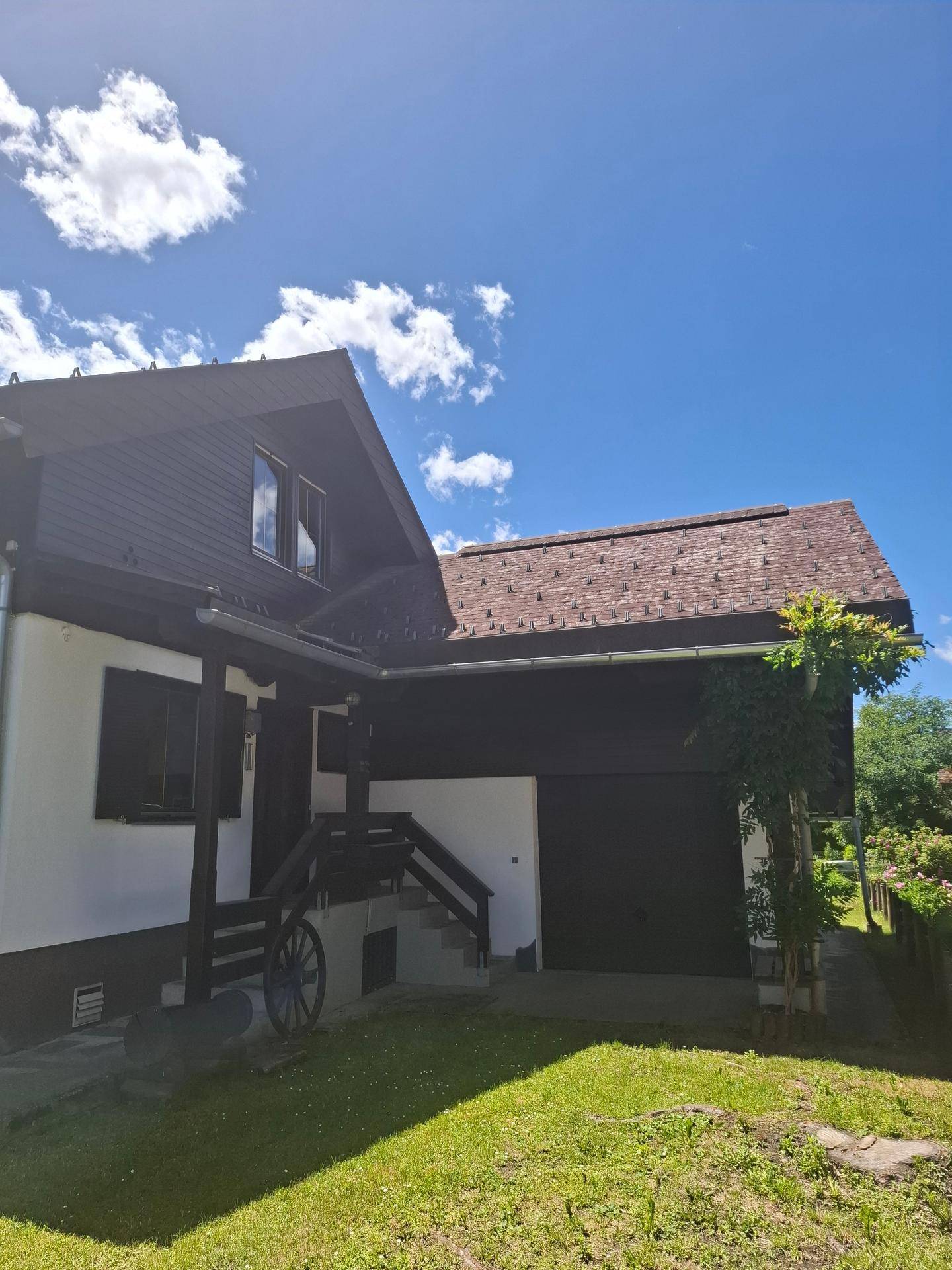 Seitenansicht des Hauses mit einer Garage und einer Außentreppe, umgeben von grünem Rasen und Bäumen.