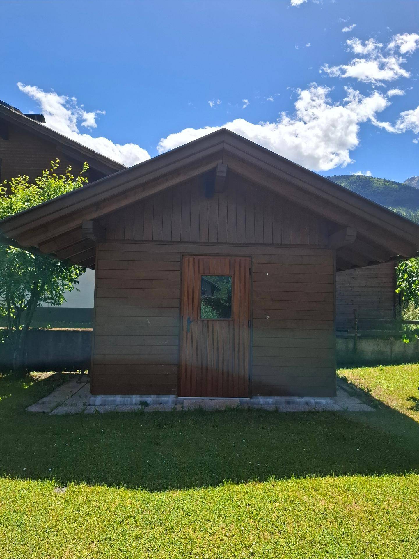 Kleines, rustikales Gartenhaus aus Holz mit Satteldach, umgeben von grünem Rasen.