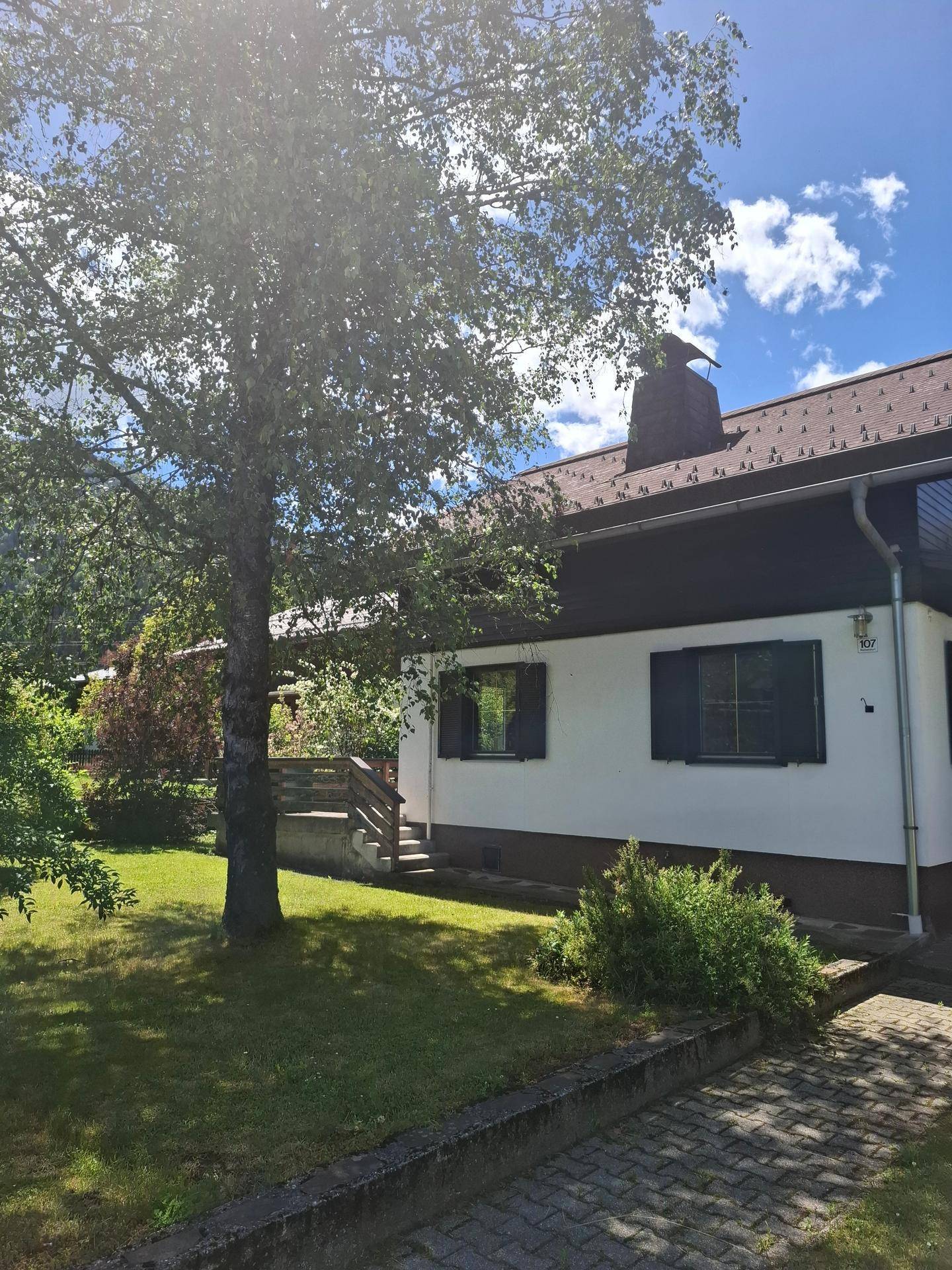 Ansicht des Hauses von der Seite mit einem großen Baum im Vorgarten und einem gepflasterten Zugang.