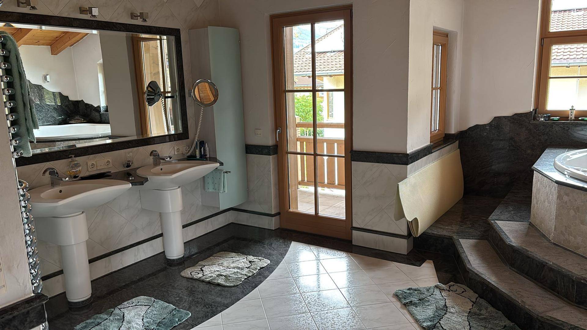 Geräumiges Badezimmer mit Doppelwaschbecken, Badewanne und Zugang zu einem kleinen Balkon.