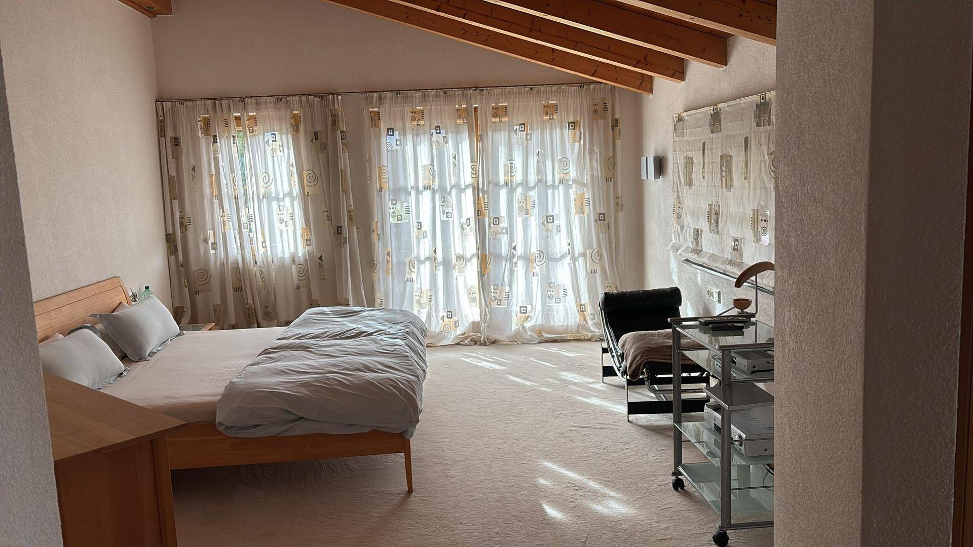 Geräumiges Schlafzimmer mit Holzbett, Teppichboden und schrägen Decken mit Holzbalken.