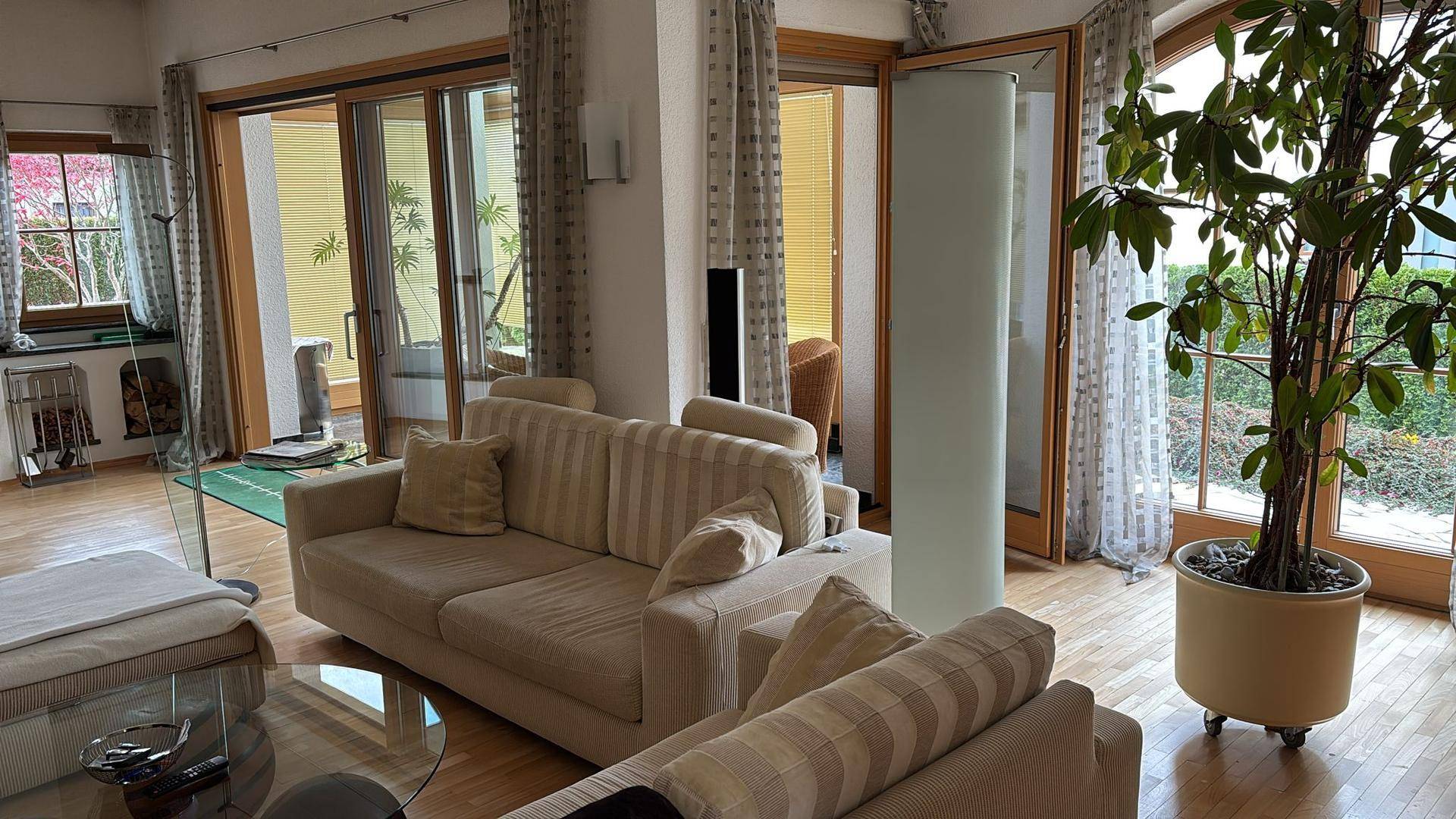Helles Wohnzimmer mit beigen Sofas, Holzboden und großen Glasfronten zur Terrasse.