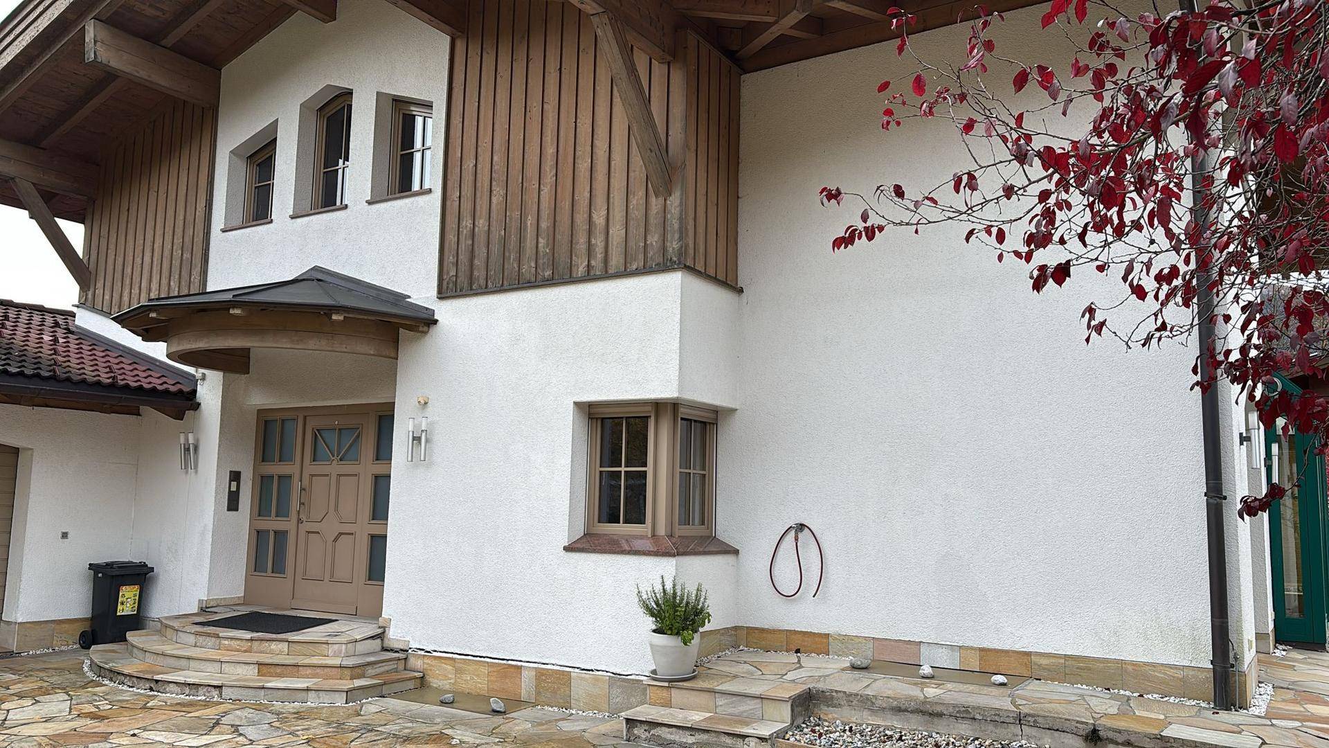 Traditionelle Hausfassade mit Holzelementen, weißem Putz und gepflastertem Eingangsbereich.