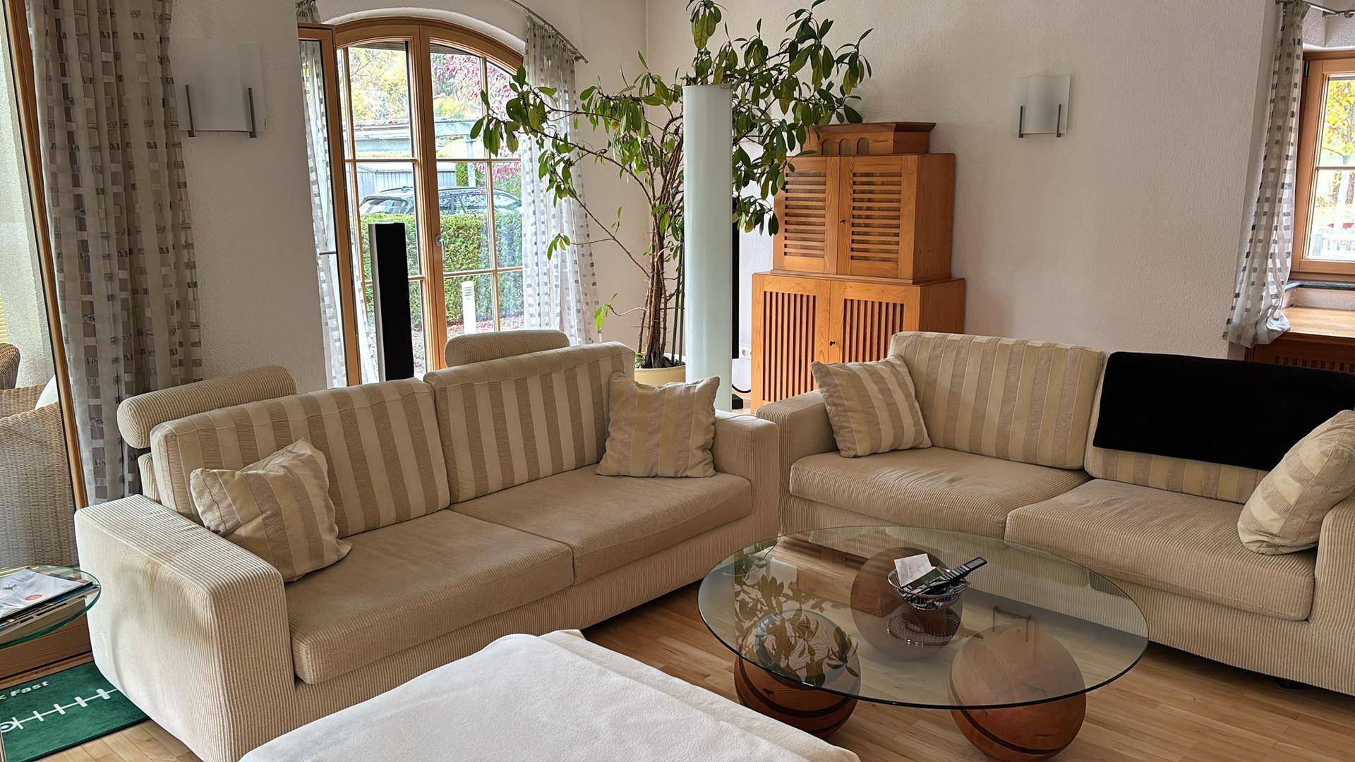 Geräumiges Wohnzimmer mit beigen Sofas, Holzboden und Pflanzen, die für eine angenehme Atmosphäre sorgen.