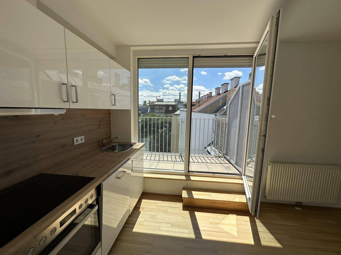 Helle Küche mit weißen Schränken, Holzakzenten und direktem Zugang zu einem sonnigen Balkon.