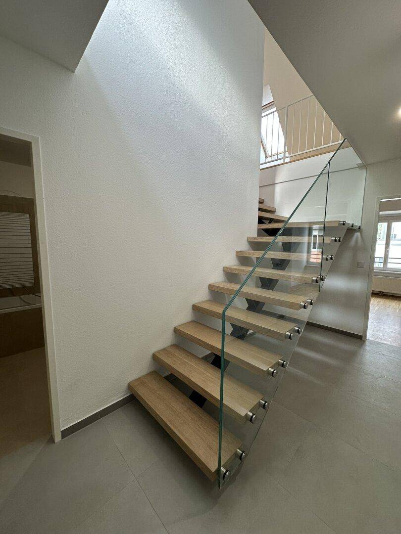 Moderner Treppenaufgang mit Holzstufen und Glasgeländer, der die Etagen verbindet.