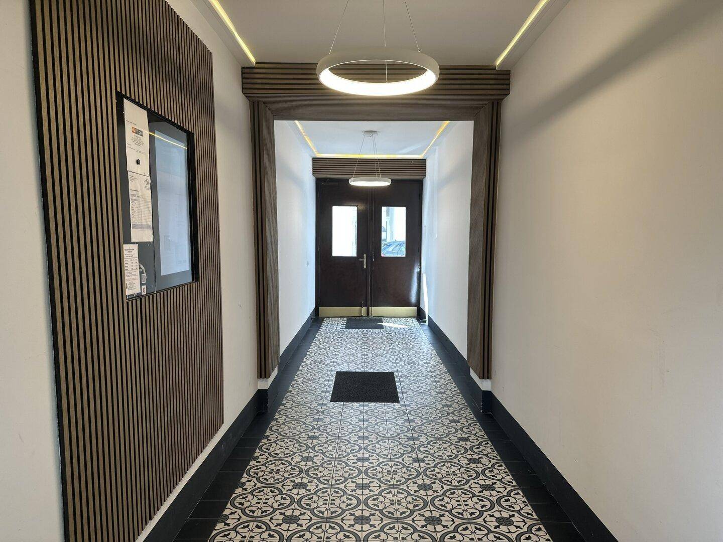 Eingangsbereich mit dekorativem Fliesenboden, Holzvertäfelung und moderner Beleuchtung.