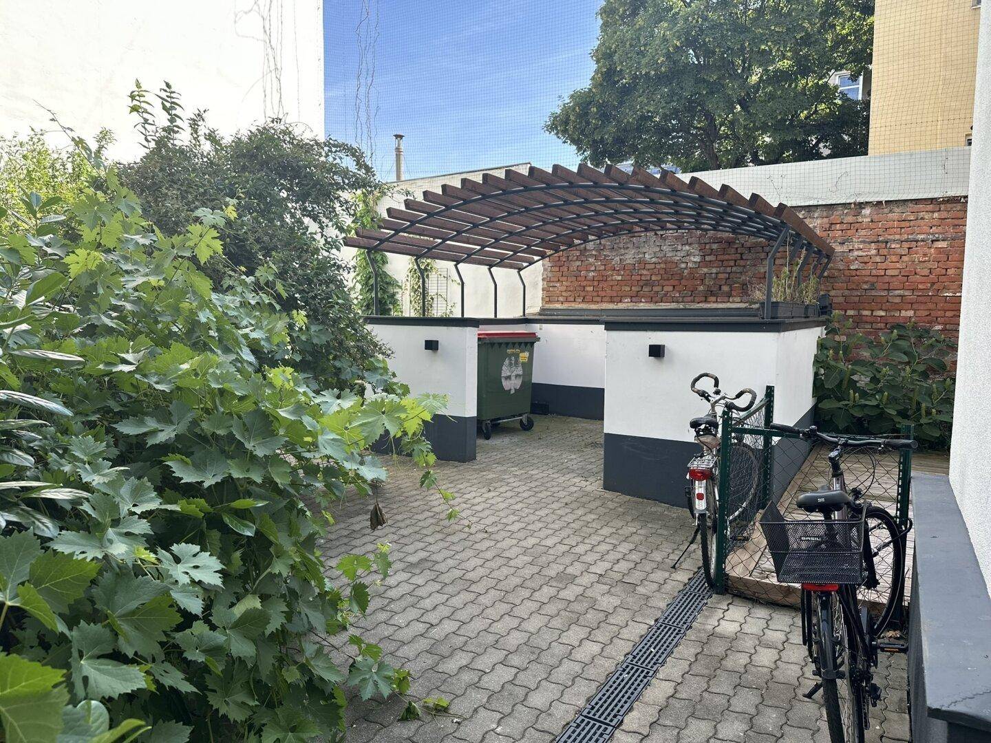 Gepflasterter Innenhof mit Fahrradabstellplätzen, Mülltonnenbereich und viel Grün.