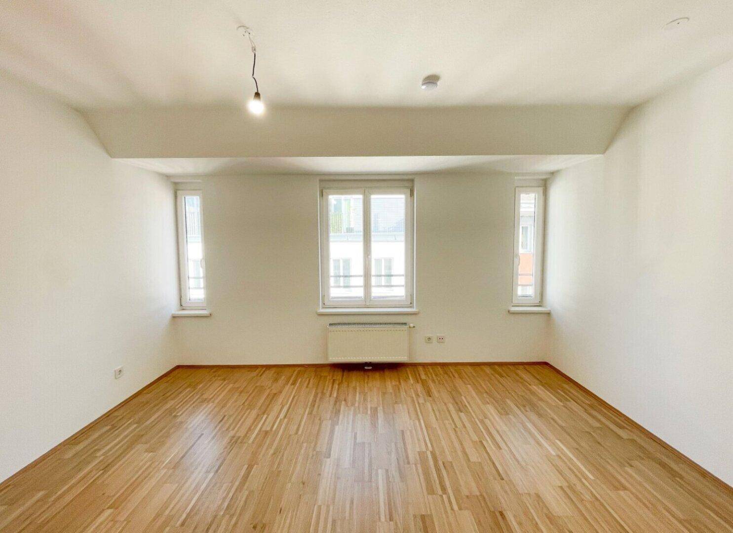 Helles Schlafzimmer mit Holzboden und hohen Fenstern, die viel natürliches Licht hereinlassen.