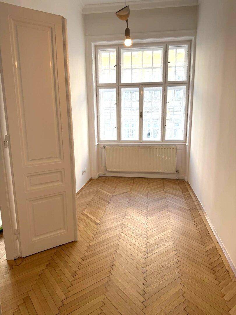 Gemütliches Zimmer mit Fischgrätparkett und großem Fenster, ideal als Schlaf- oder Arbeitszimmer.