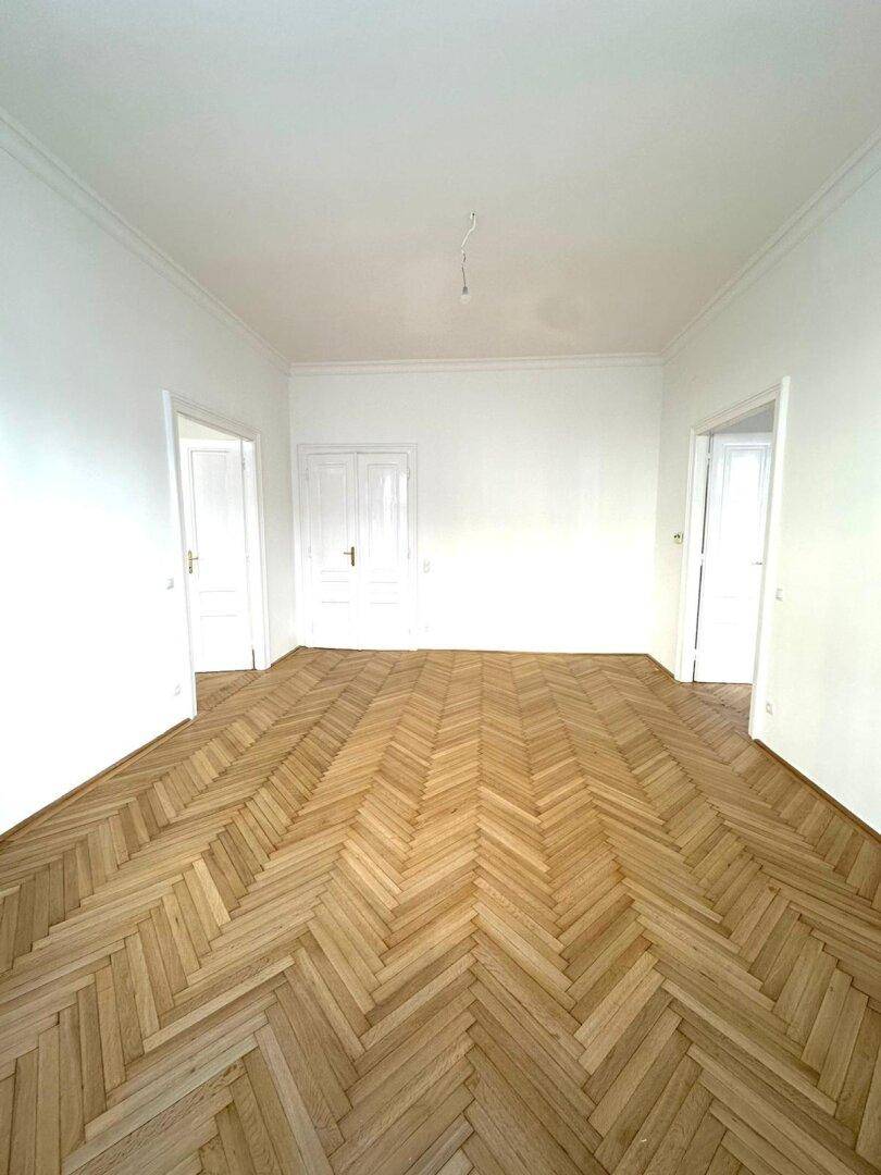 Geräumiges Zimmer mit Fischgrätparkett und hohen Decken, bereit für neue Bewohner.