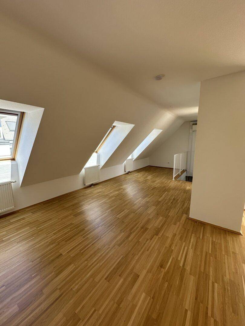 Heller Wohnraum mit Holzboden, Dachschrägen und mehreren Dachfenstern für viel Tageslicht.