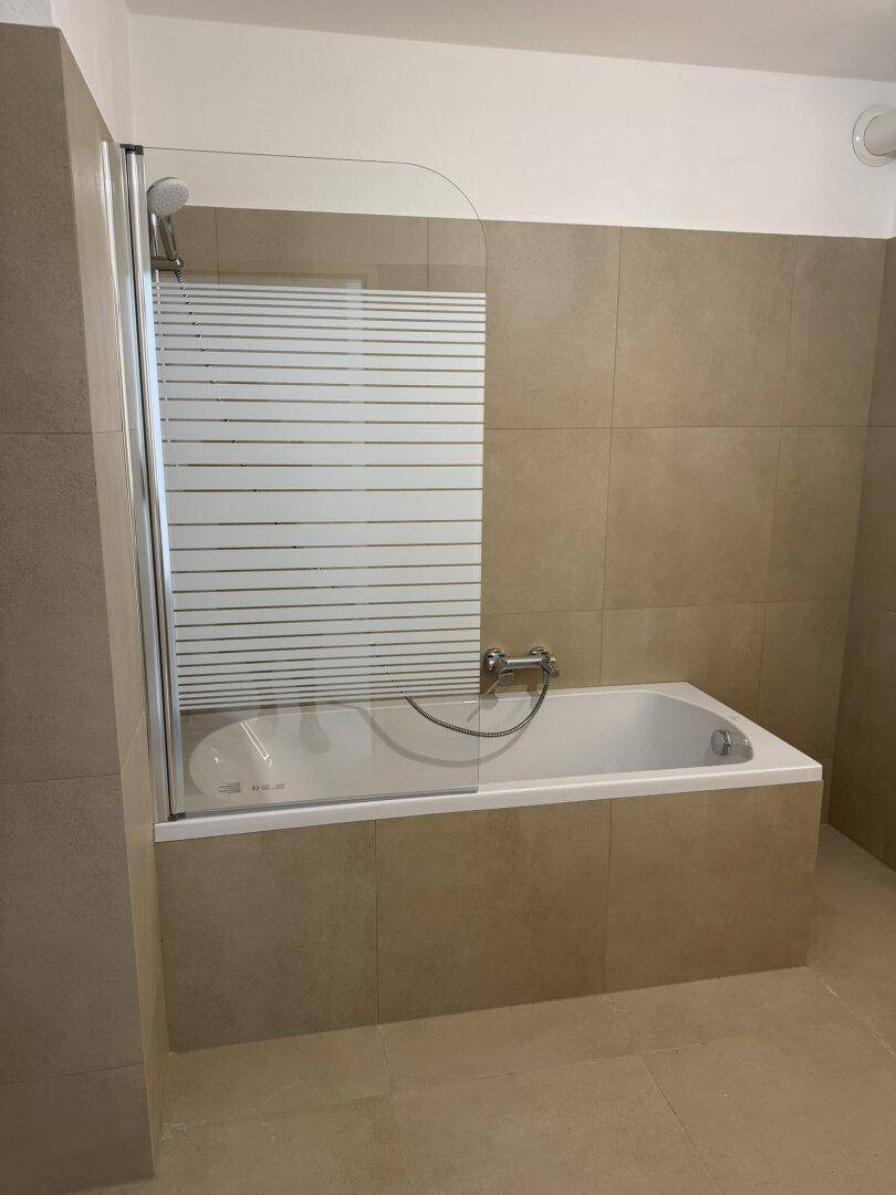 Modernes Badezimmer mit Badewanne, Duschabtrennung und beigefarbenen Fliesen.