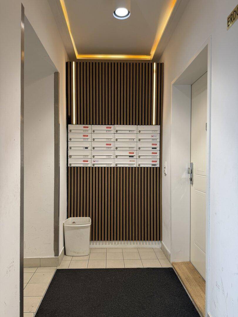 Eingangsbereich mit Briefkästen, Holzvertäfelung und moderner Deckenbeleuchtung.
