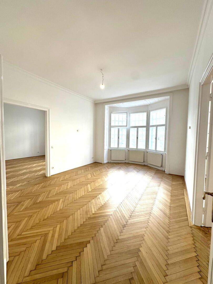 Helles Zimmer mit Fischgrätparkett und einem charmanten Erkerfenster, das viel Tageslicht bietet.