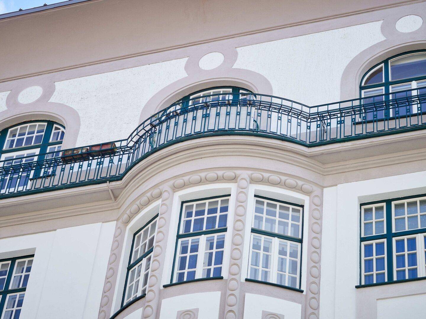 Detailansicht einer eleganten Fassade mit geschwungenem Balkon und verzierten Fenstern.