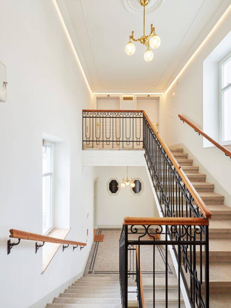 Elegantes Treppenhaus mit schmiedeeisernem Geländer, Holzhandläufen und dekorativer Deckenbeleuchtung.