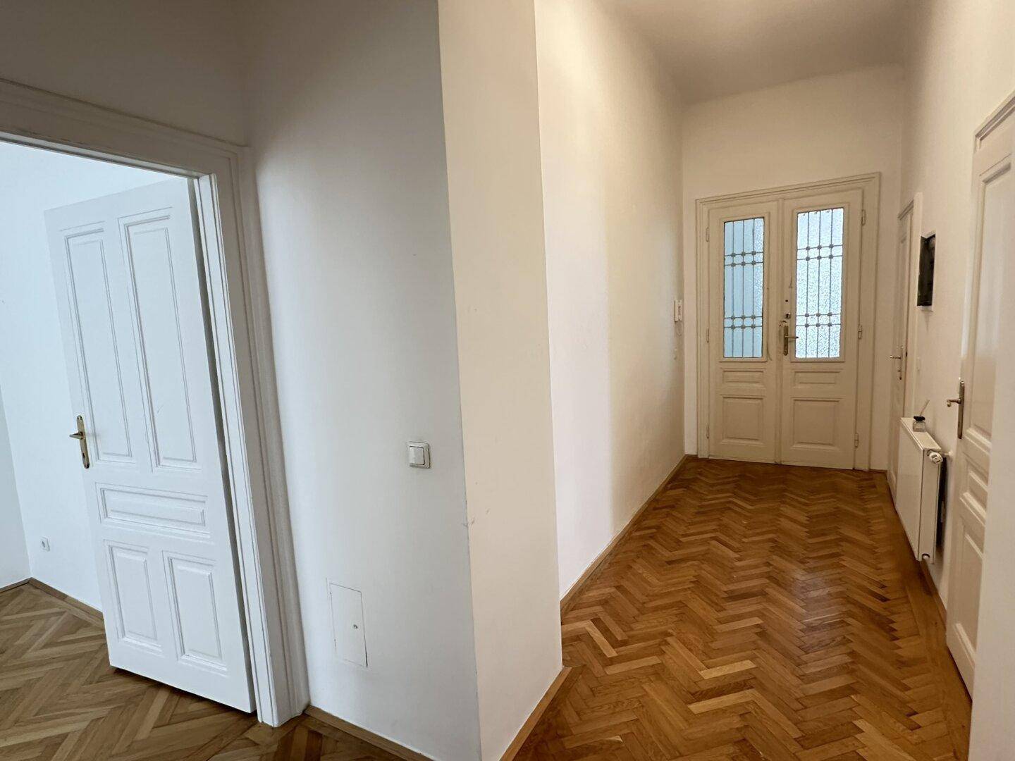 Heller Flur mit Fischgrätparkett und einer stilvollen Eingangstür mit Glaseinsätzen.