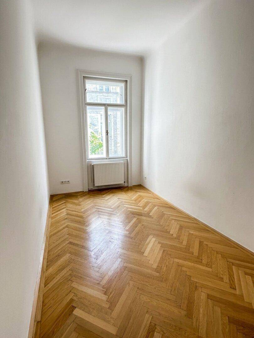 Kleineres Zimmer mit hellem Fischgrätparkett und einem Fenster, ideal als Schlaf- oder Arbeitszimmer.