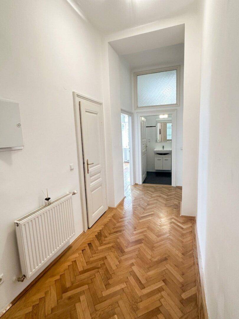 Langer Flur mit Fischgrätparkett, der zu einem Badezimmer am Ende führt.