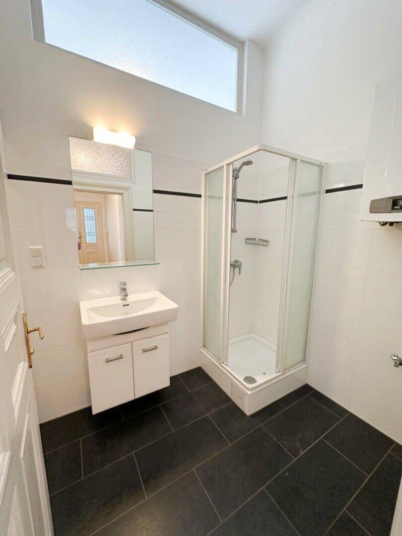 Modernes Badezimmer mit Duschkabine, Waschbecken und dunklem Fliesenboden.