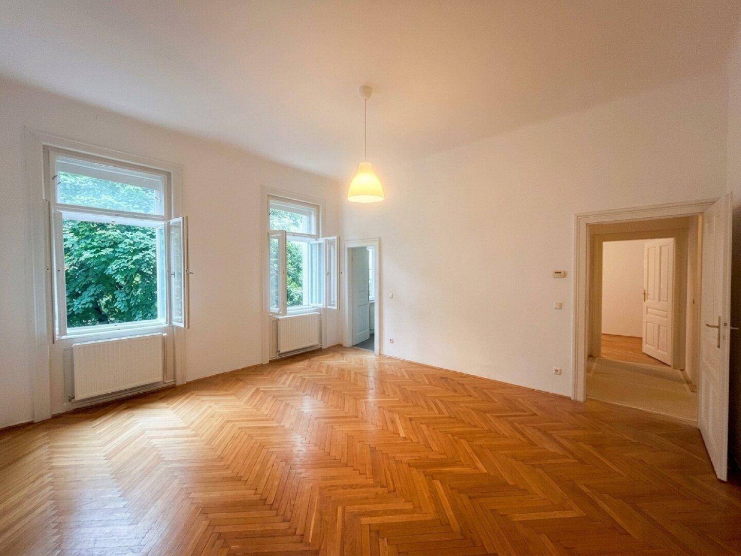Geräumiges Wohnzimmer mit klassischem Fischgrätparkett und mehreren Türen zu angrenzenden Räumen.