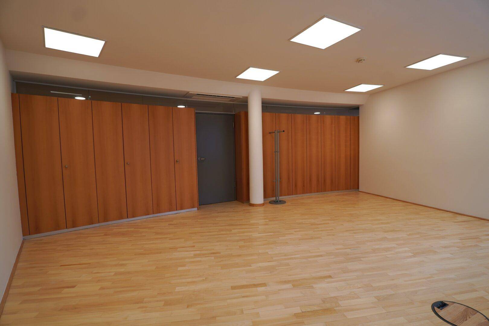 Leerer Büroraum mit Holzparkettboden und integrierten Holzschränken entlang der Wand.