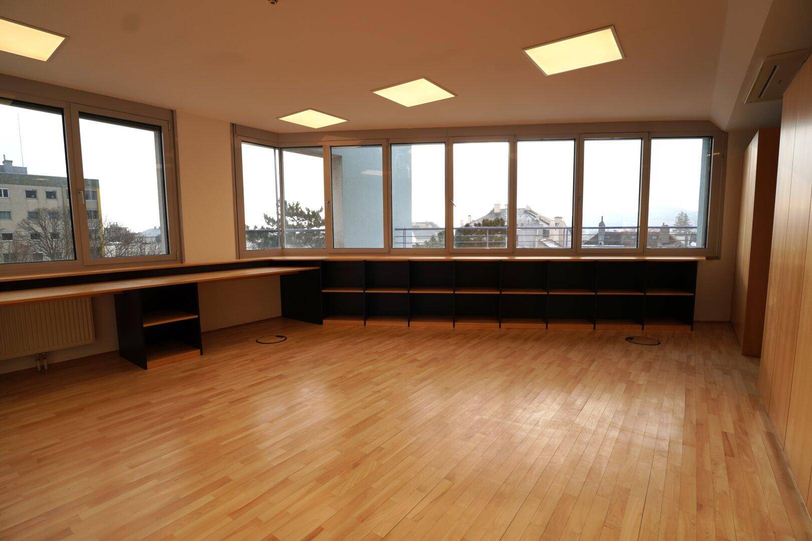 Leerer Büroraum mit großen Fenstern, die einen weiten Blick über die Stadt bieten.