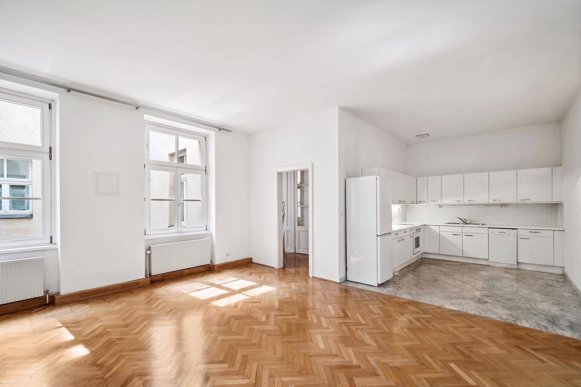 Geräumiger Wohnbereich mit integrierter weißer Küche und Fischgrätparkett, ideal für offenes Wohnen.