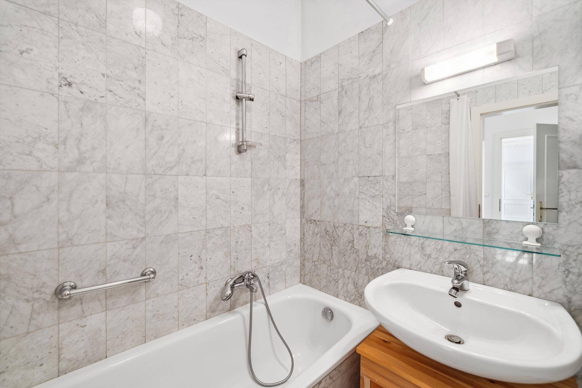 Modernes Badezimmer mit Marmorfliesen, Badewanne und Einzelwaschbecken, hell und gepflegt.