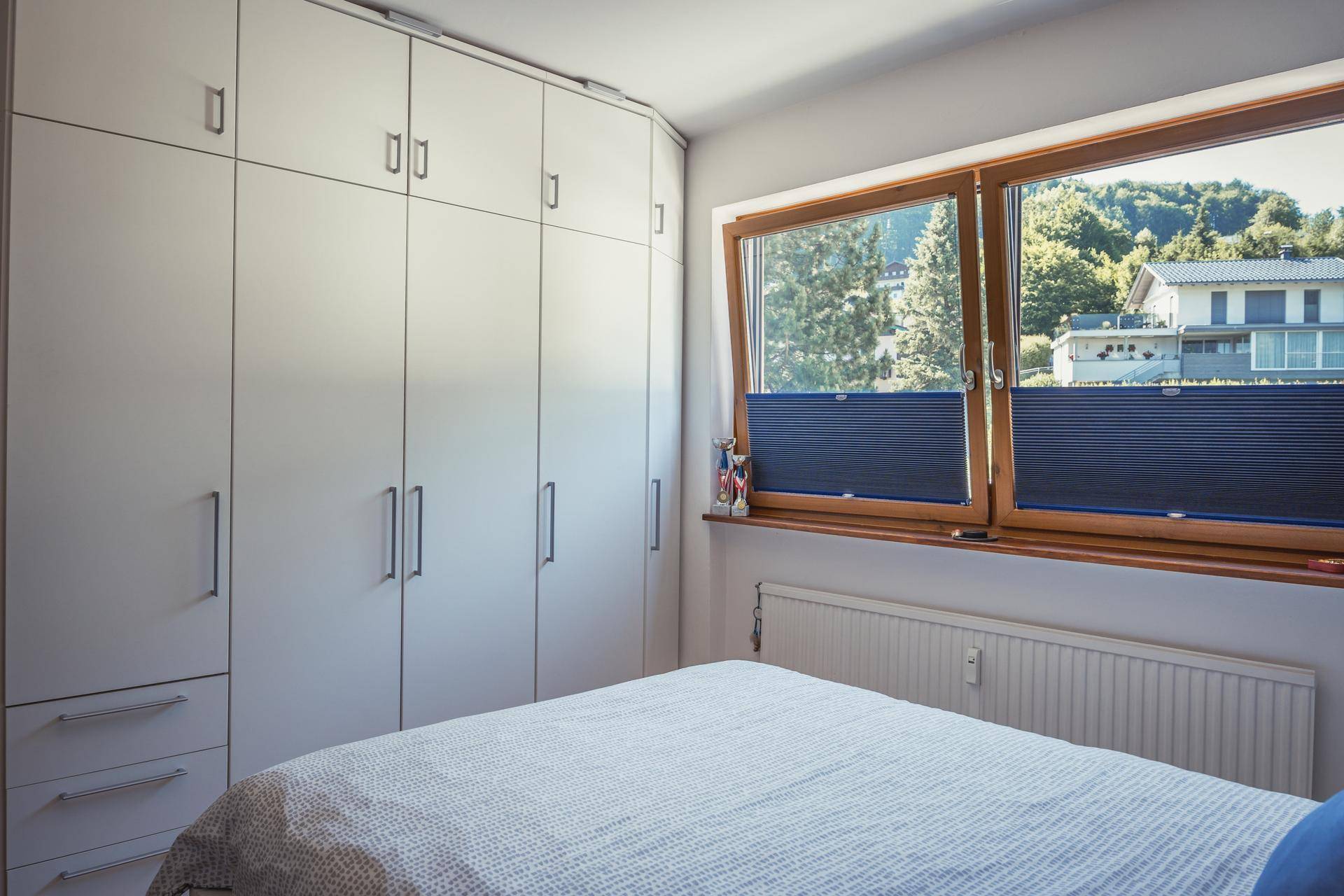 Helles Schlafzimmer mit großem Einbauschrank und Fensterblick auf die umliegende Wohngegend.