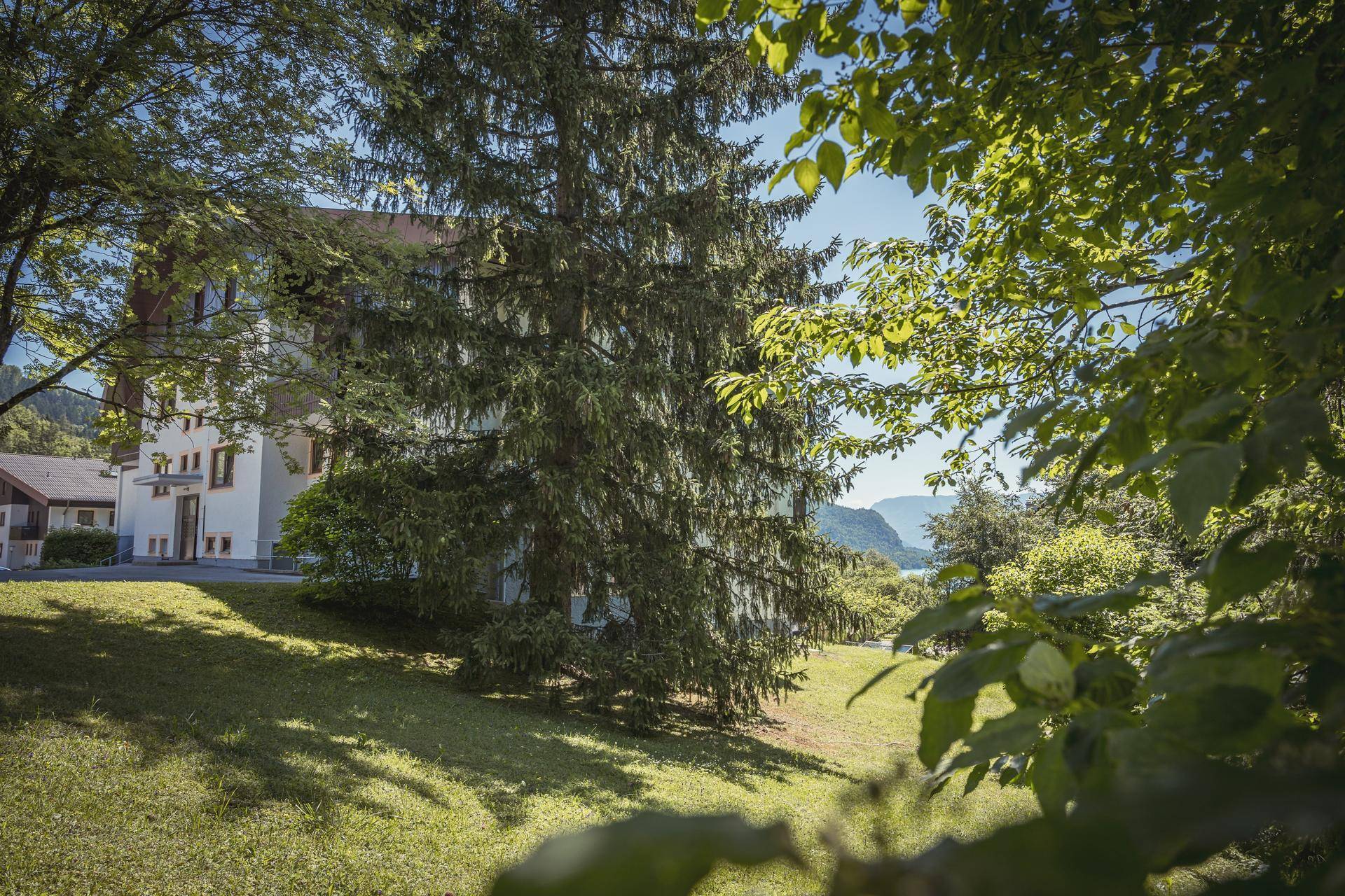 Gebäudeansicht durch Bäume hindurch, mit weitem Blick auf die Landschaft und den See in der Ferne.