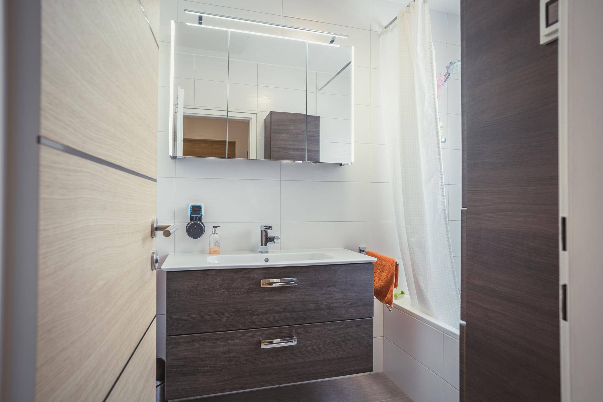 Modernes Badezimmer mit Waschtisch, Spiegelschrank und Badewanne mit Duschvorhang.